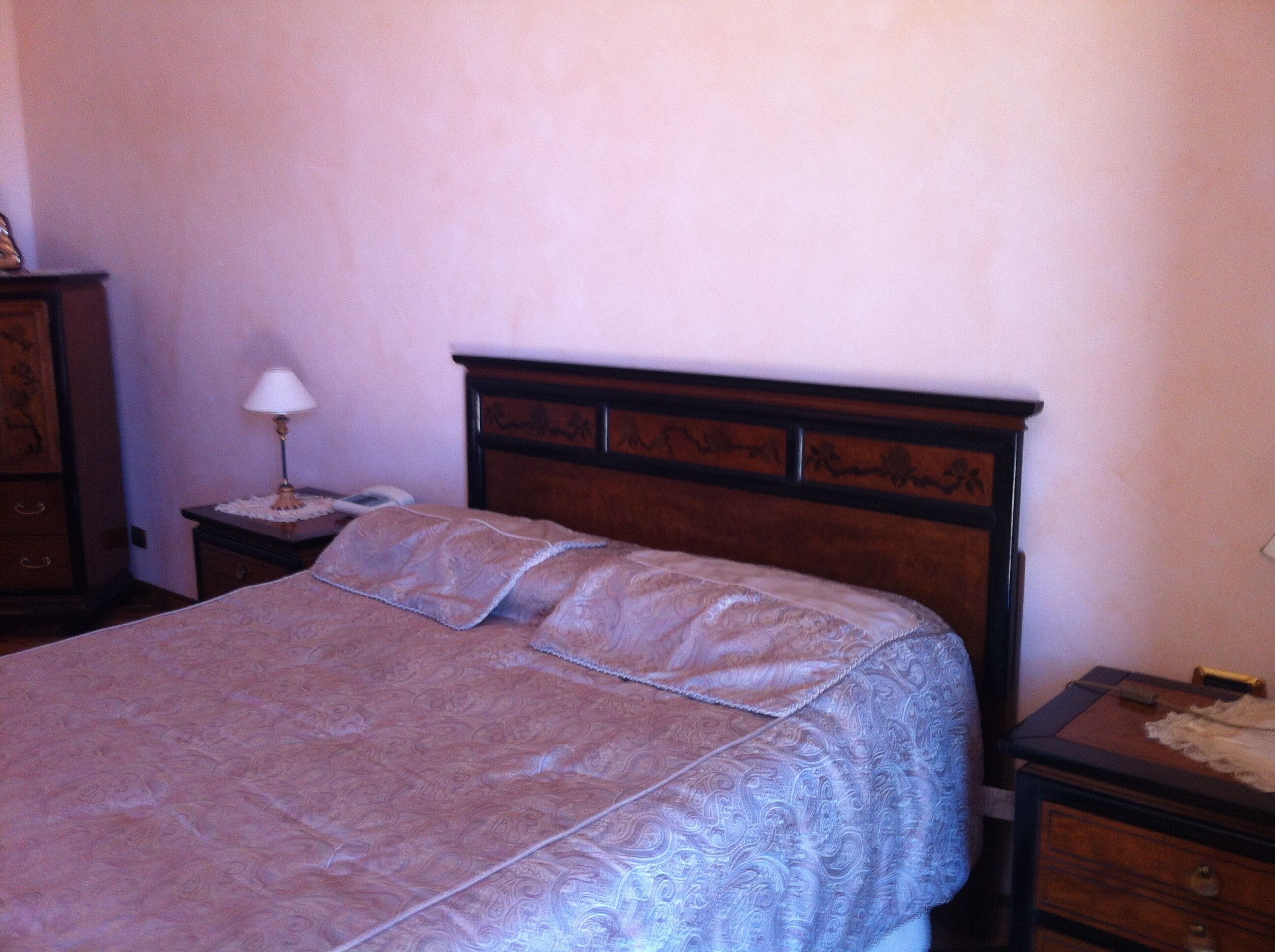 A bedroom with a wooden headboard, a bedside table with a lamp, and a nightstand.