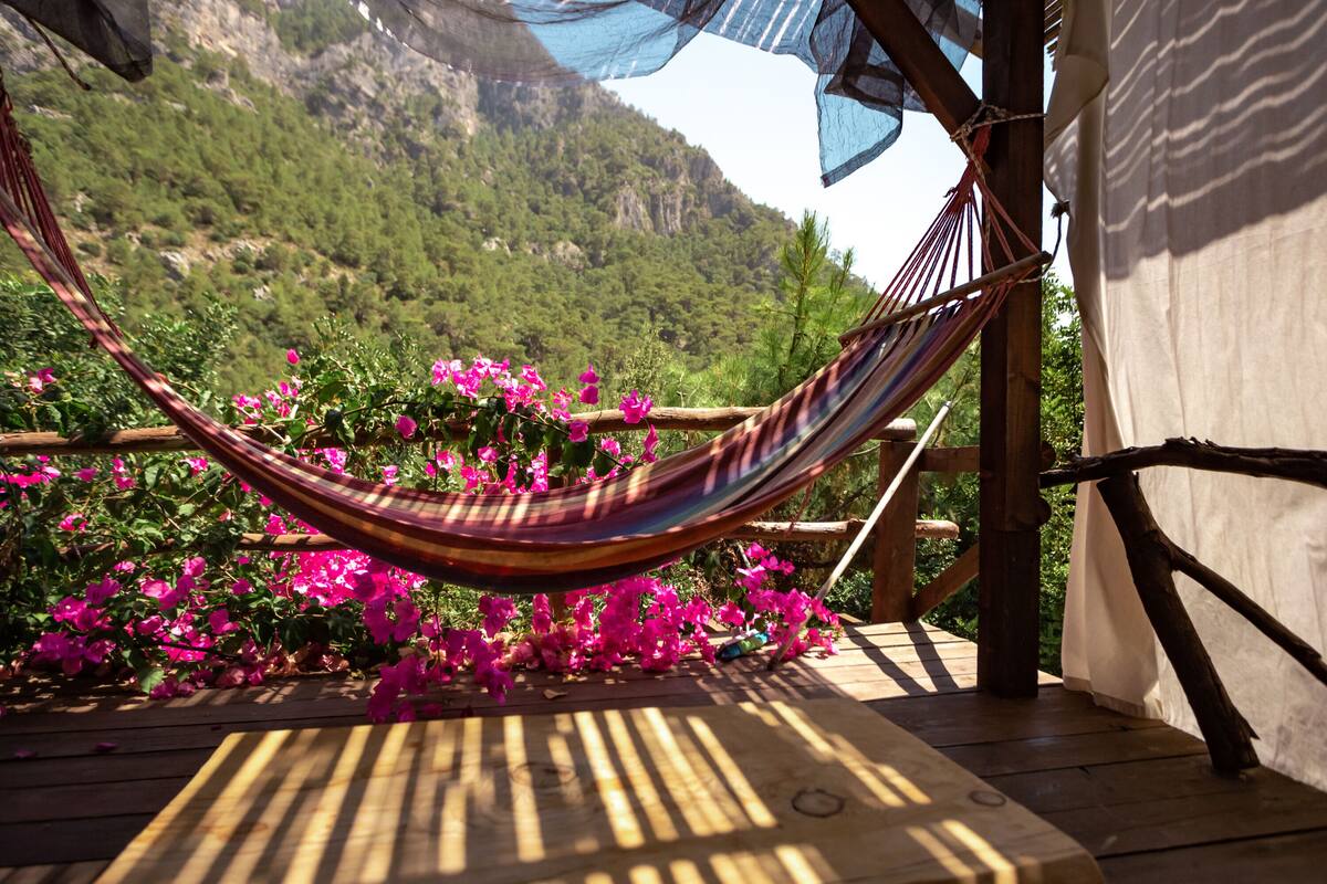 A hammock on a wooden deck with pink flowers and a mountainous backdrop.
