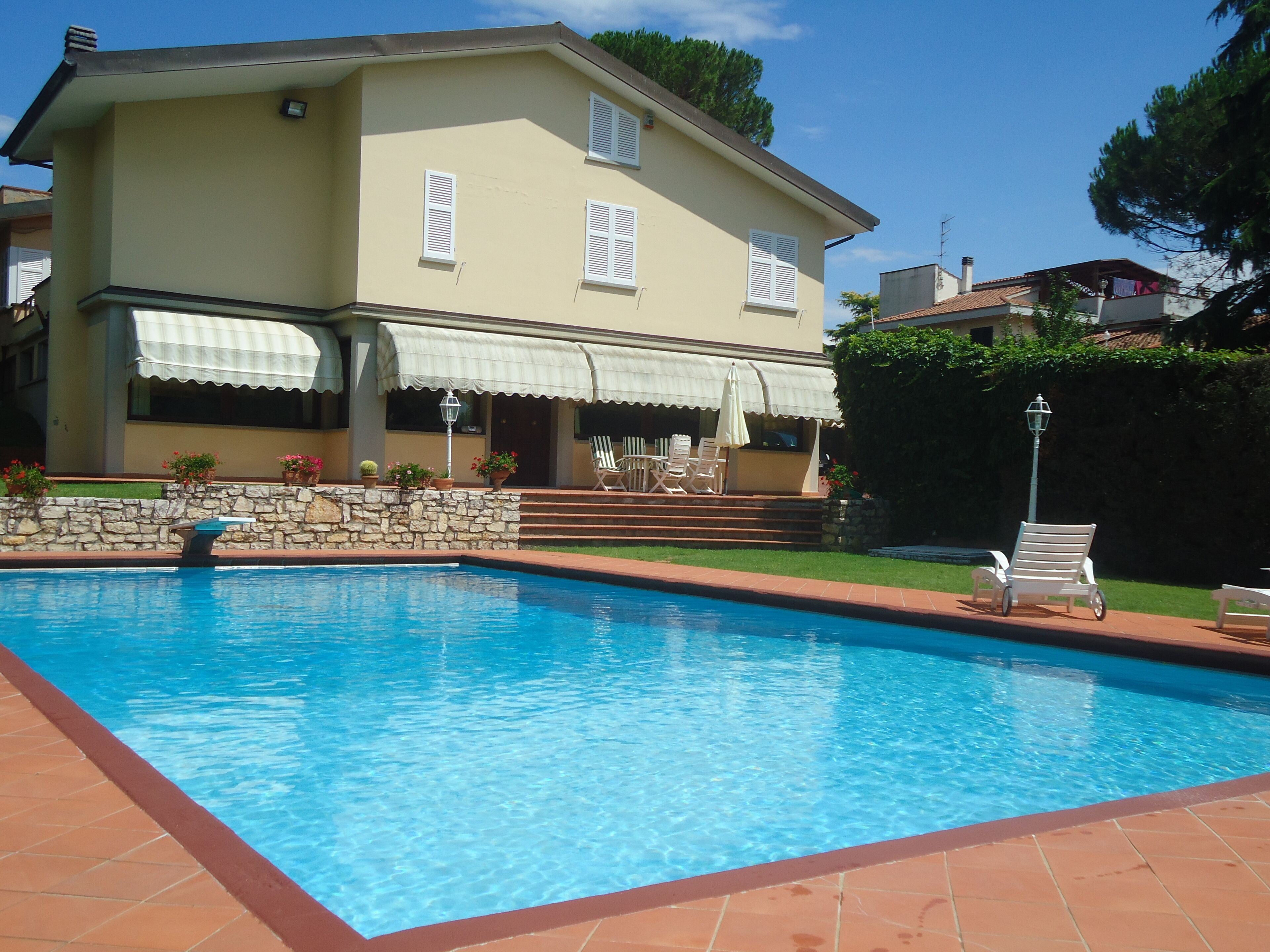 Ein zweistöckiges Haus mit Swimmingpool, Steinmauer und Gartenmöbeln.