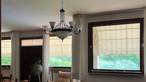 Ein großzügiger Wohnraum mit großem Fenster, einer Chandelierleuchtre und einem Essbereich mit Stühlen und Tisch.