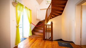 A wooden staircase with a red rope barrier, a wooden handrail, and a doormat with text.