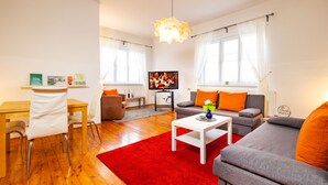 A modern living room with a wooden floor, a red rug, a grey sofa, a white coffee table, and a television.