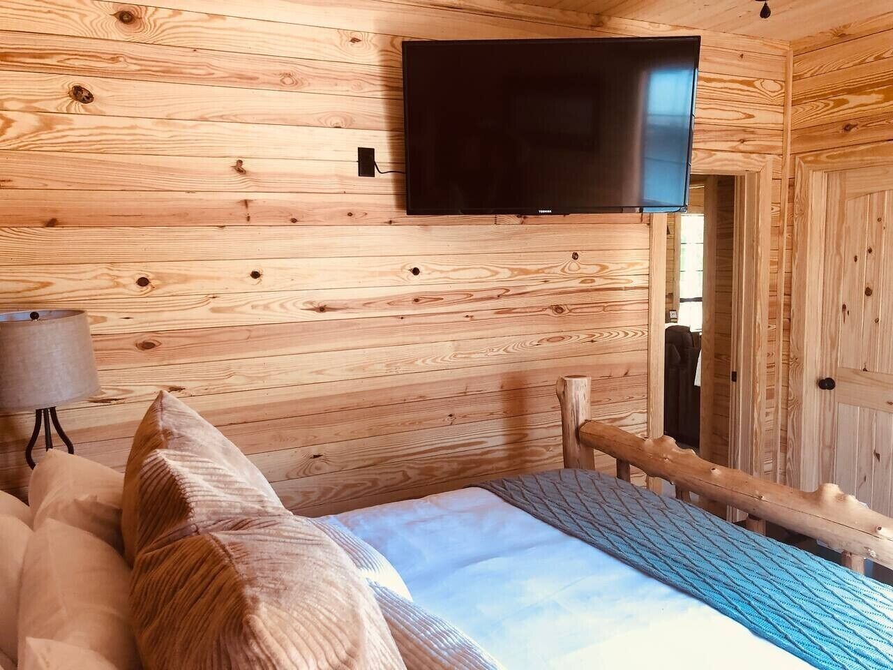 Een houten blokhut van binnen met een bed, een bevestigde televisie en een lamp.