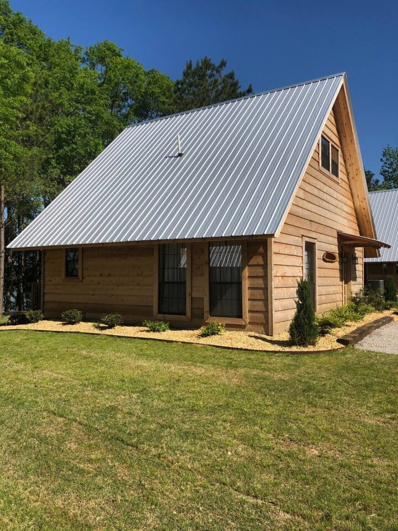 Une cabane en bois avec un toit métallique à pente, un porche à l’avant et une pelouse bien entretenue.
