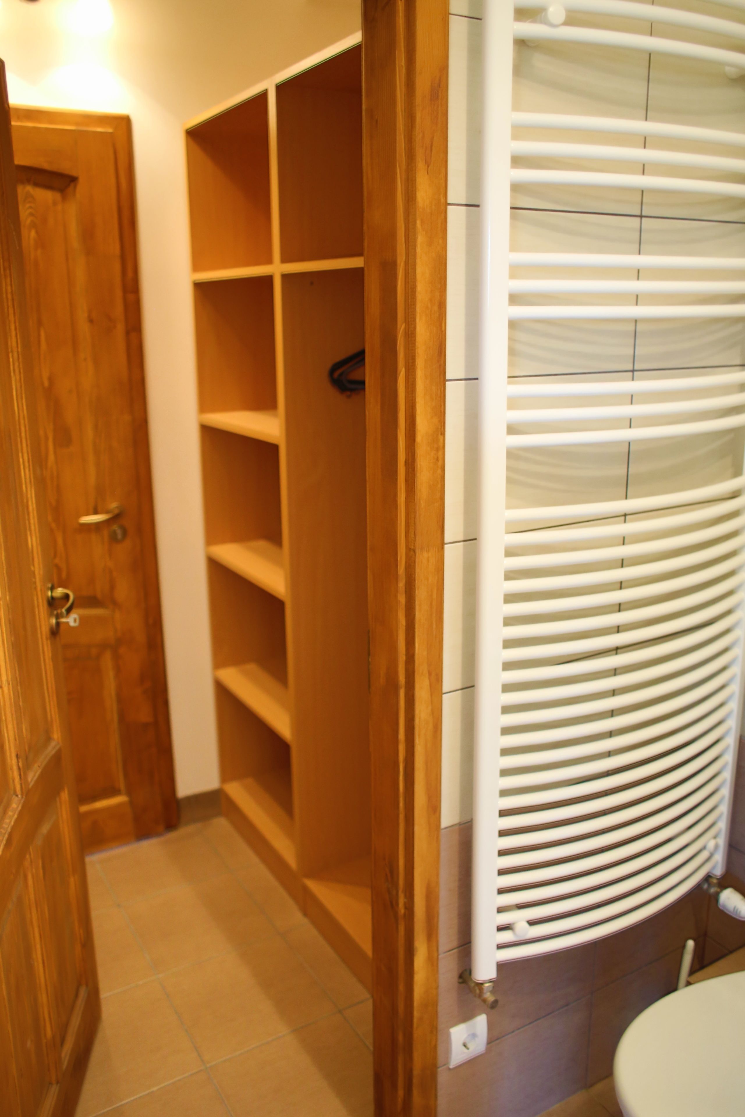 Un baño con puerta de madera, radiador blanco y suelo de baldosas.