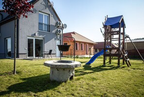 A residential area with a modern house, a stone well, and a wooden play structure with a slide. - Szabolcs Apartments (Demjén)