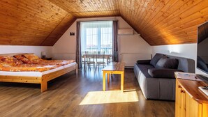 A cozy attic bedroom with a wooden ceiling, a bed, a sofa, a dining table, and a TV. - Szabolcs Apartments (Demjén)