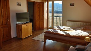 A bedroom with a wooden bed, a television on a wooden cabinet, and a view of a mountainous landscape through a sliding glass door. - Szabolcs Apartments (Demjén)