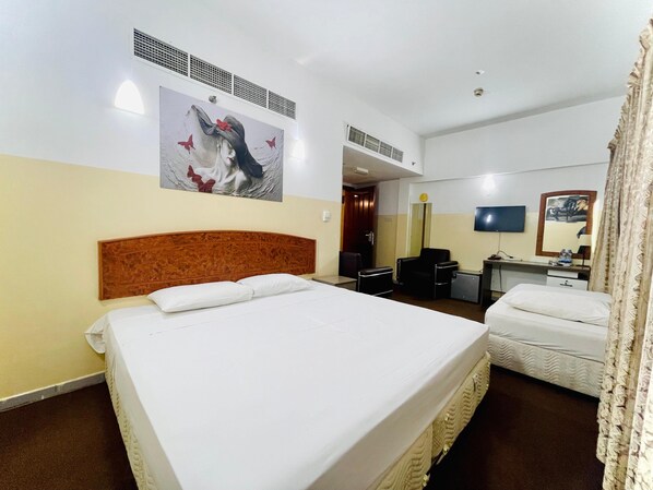 Une chambre d’hôtel avec un grand lit, un lit plus petit, un bureau, une chaise, une télévision et un miroir.