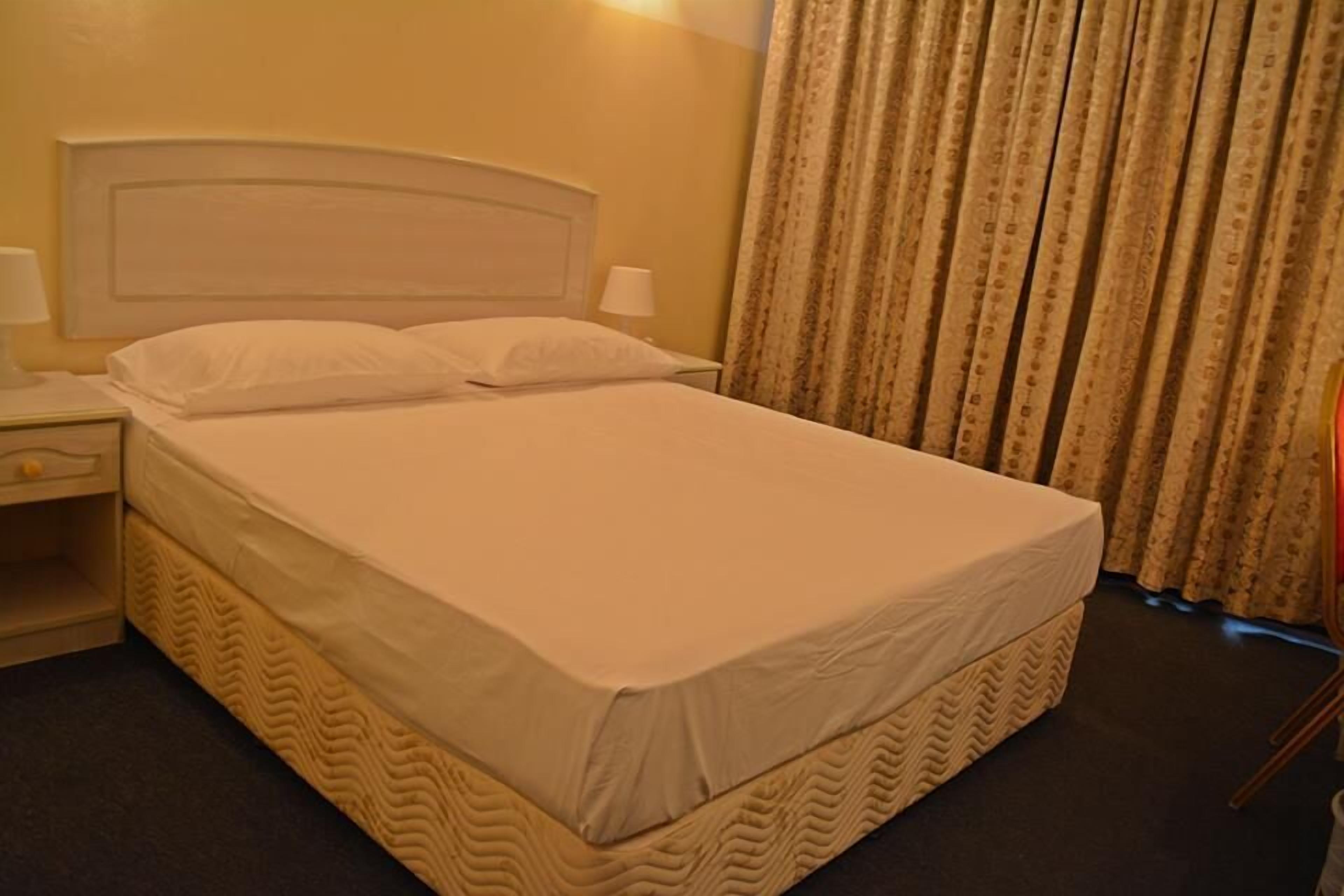 A hotel room with a large bed, a nightstand, a lamp, and a curtain.