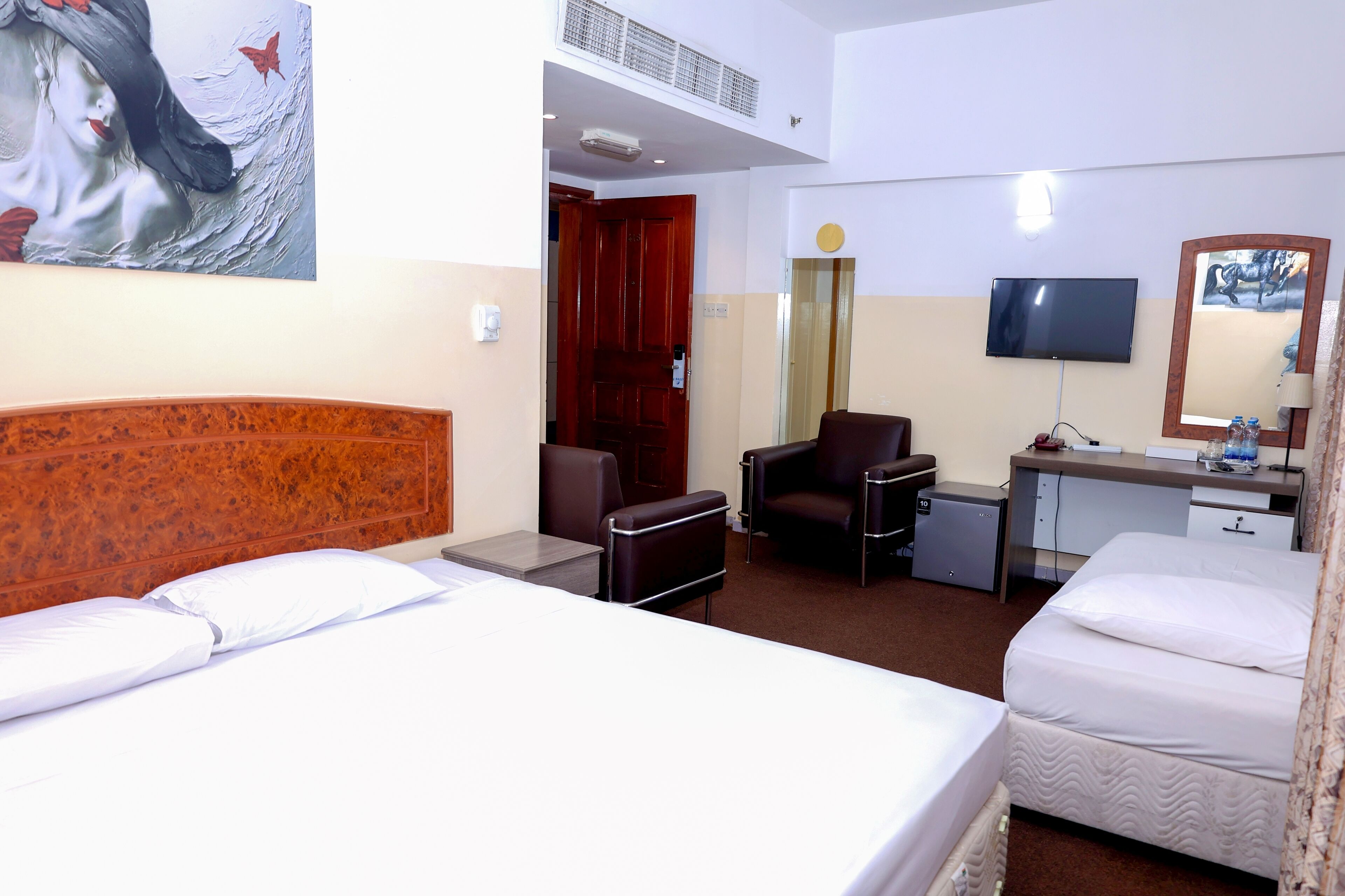 A hotel room with two beds, a desk, a chair, a TV, and a small refrigerator.