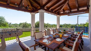An outdoor patio with a wooden table set for dining, surrounded by chairs, and a foosball table.