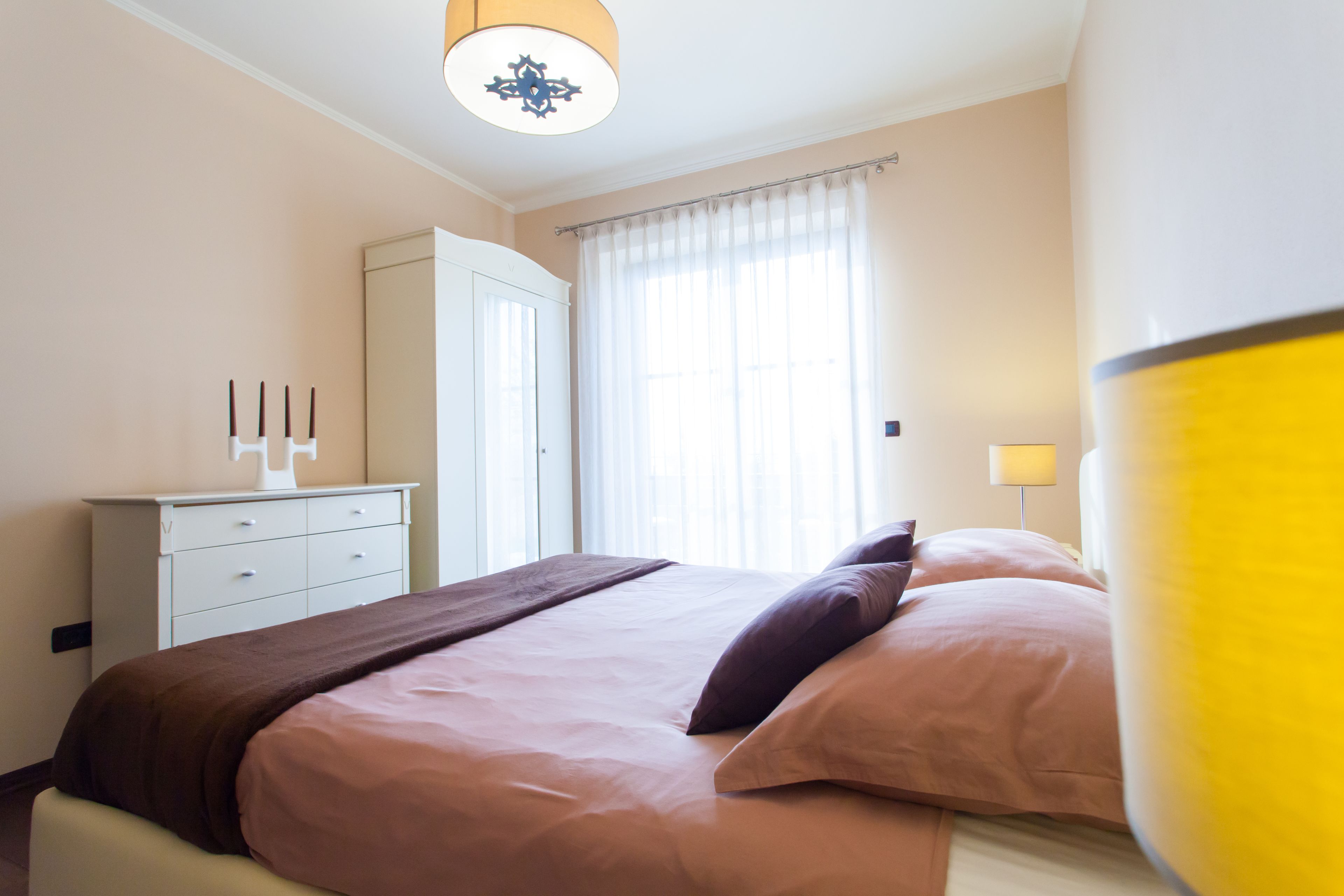 Une chambre d’hôtel avec un lit, une commode, un miroir et une fenêtre avec des rideaux.