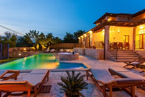 A pool area with lounge chairs, a hot tub, and a covered patio with outdoor seating.