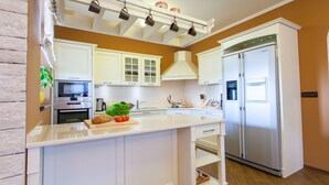 A modern kitchen with white cabinetry, a stainless steel refrigerator, and a central island with a plant and vegetables.