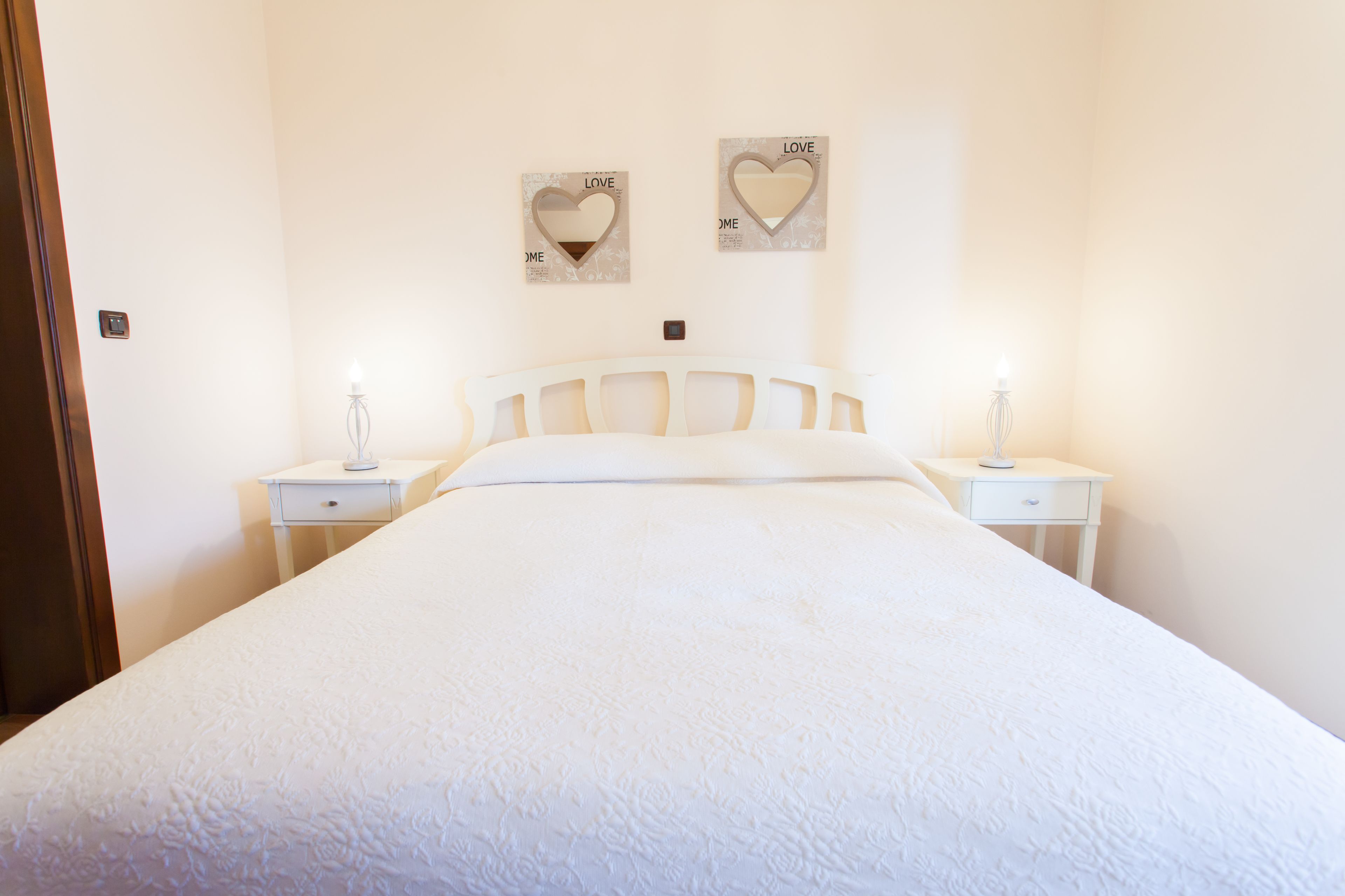 Een slaapkamer met een bed, twee nachtkastjes en twee hartvormige decoraties aan de muur met de tekst 'LOVE'.