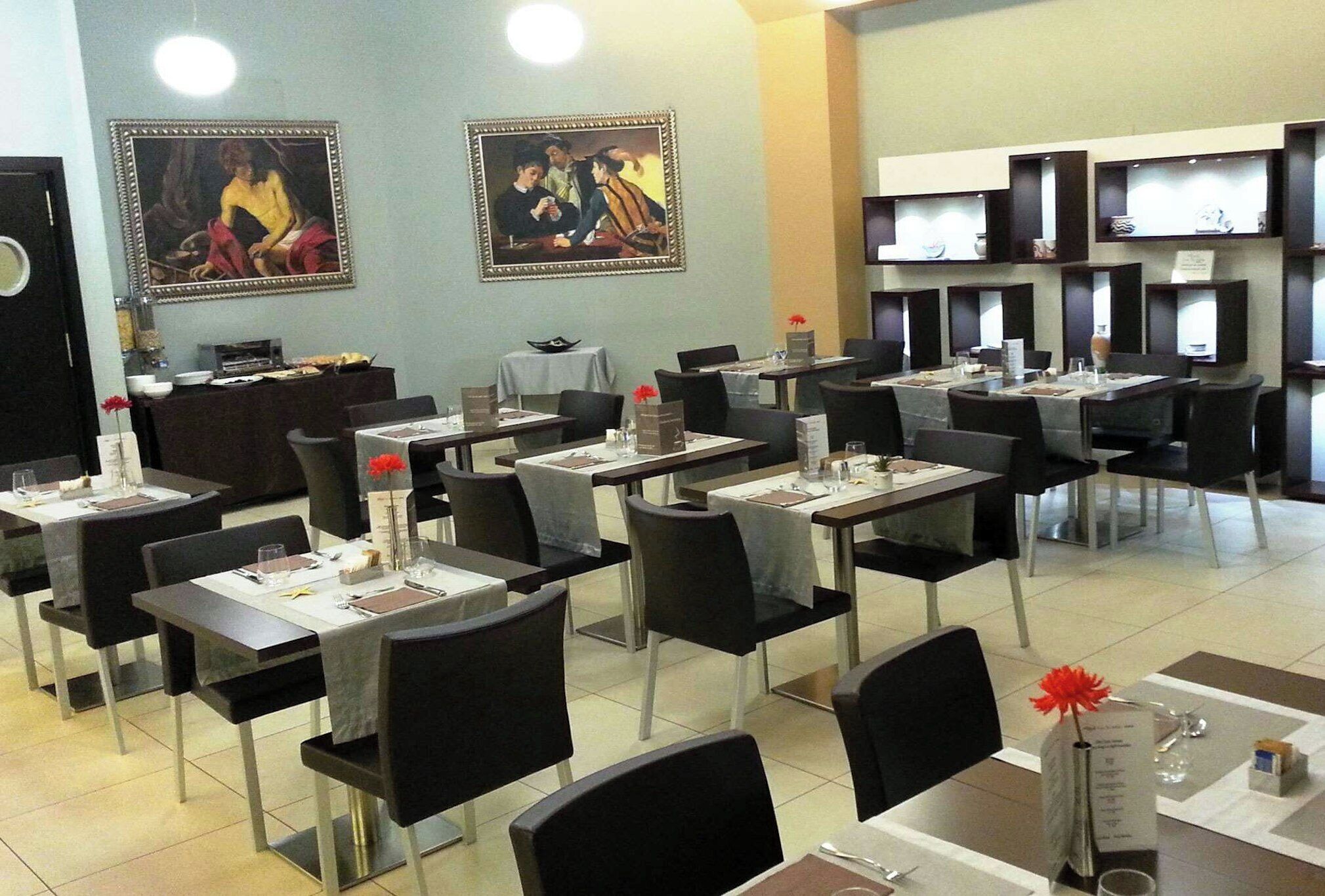 Una sala ristorante con tavoli apparecchiati, sedie e opere d'arte alle pareti.