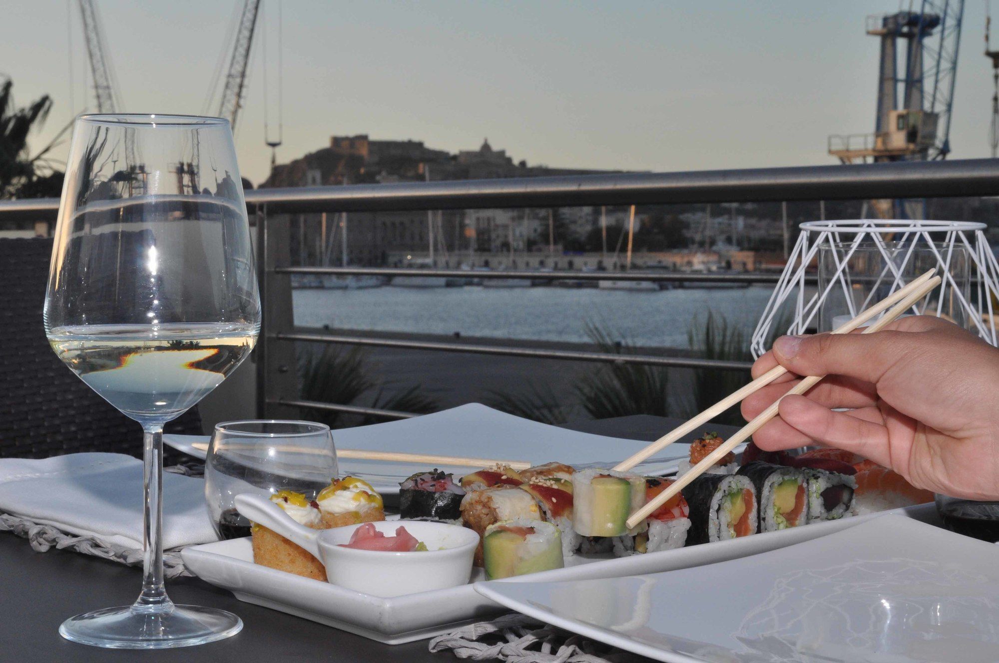 A table with sushi, a glass of white wine, and chopsticks.