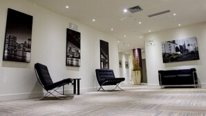 A modern lobby with two black lounge chairs, a black sofa, and cityscape paintings on the walls. - La Bussola Hotel (Milazzo)