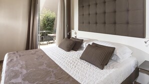 A hotel room with a large bed, a headboard, a bedside table, and a view of an outdoor area with a table and chairs. - La Bussola Hotel (Milazzo)