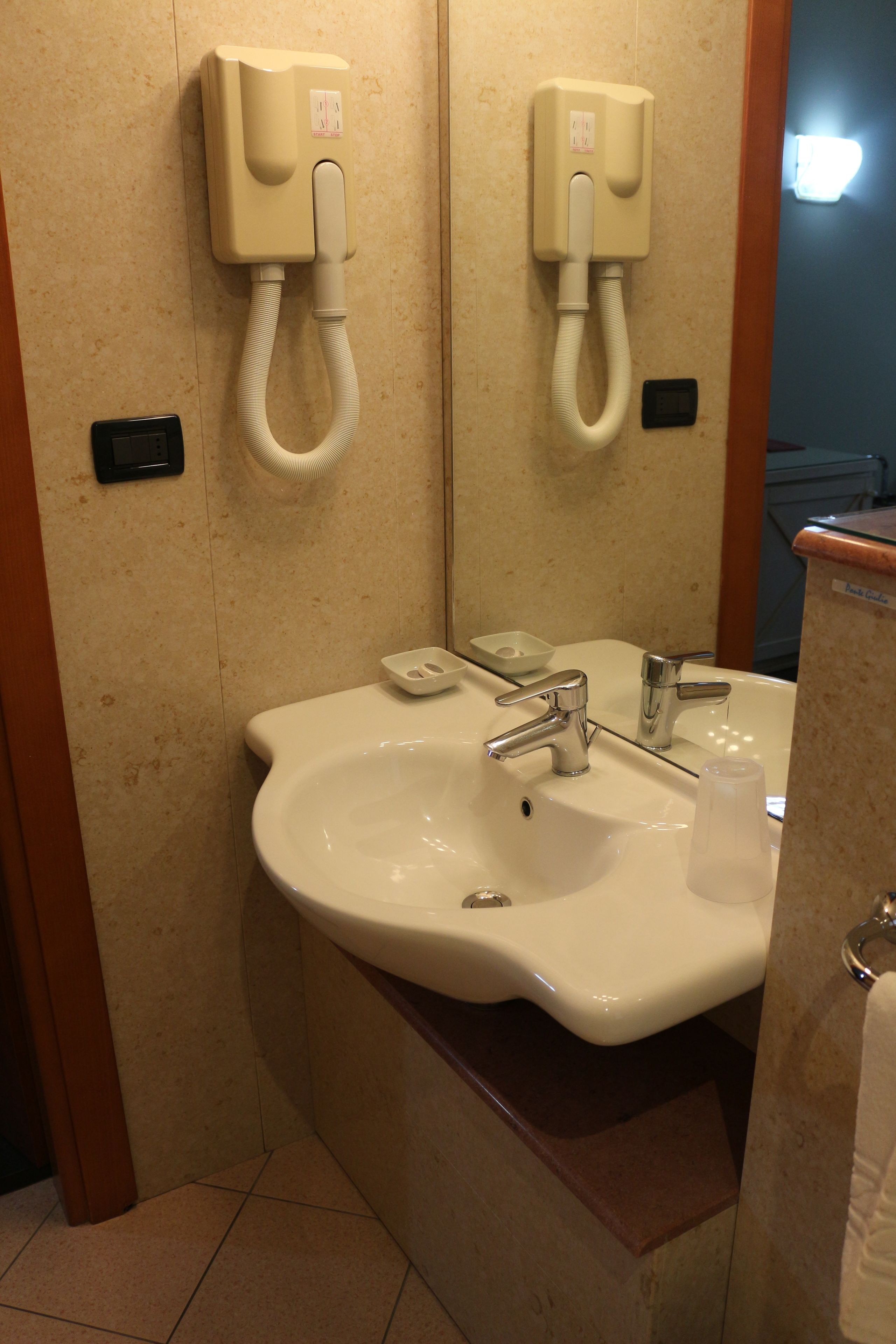 A bathroom with a sink, two faucets, a soap dish, and a hand dryer.