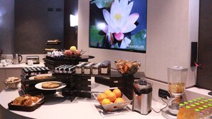 Montaje tipo bufé con diversos alimentos, una máquina de café y un bol de frutas.