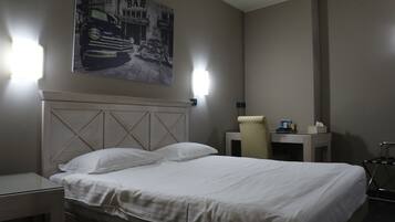 A hotel room with a bed, nightstand, lamp, chair, and a wall-mounted artwork.