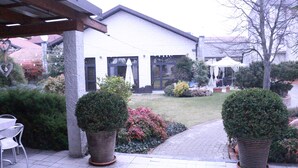 Un edificio con un patio cubierto, plantas en macetas y mobiliario exterior.