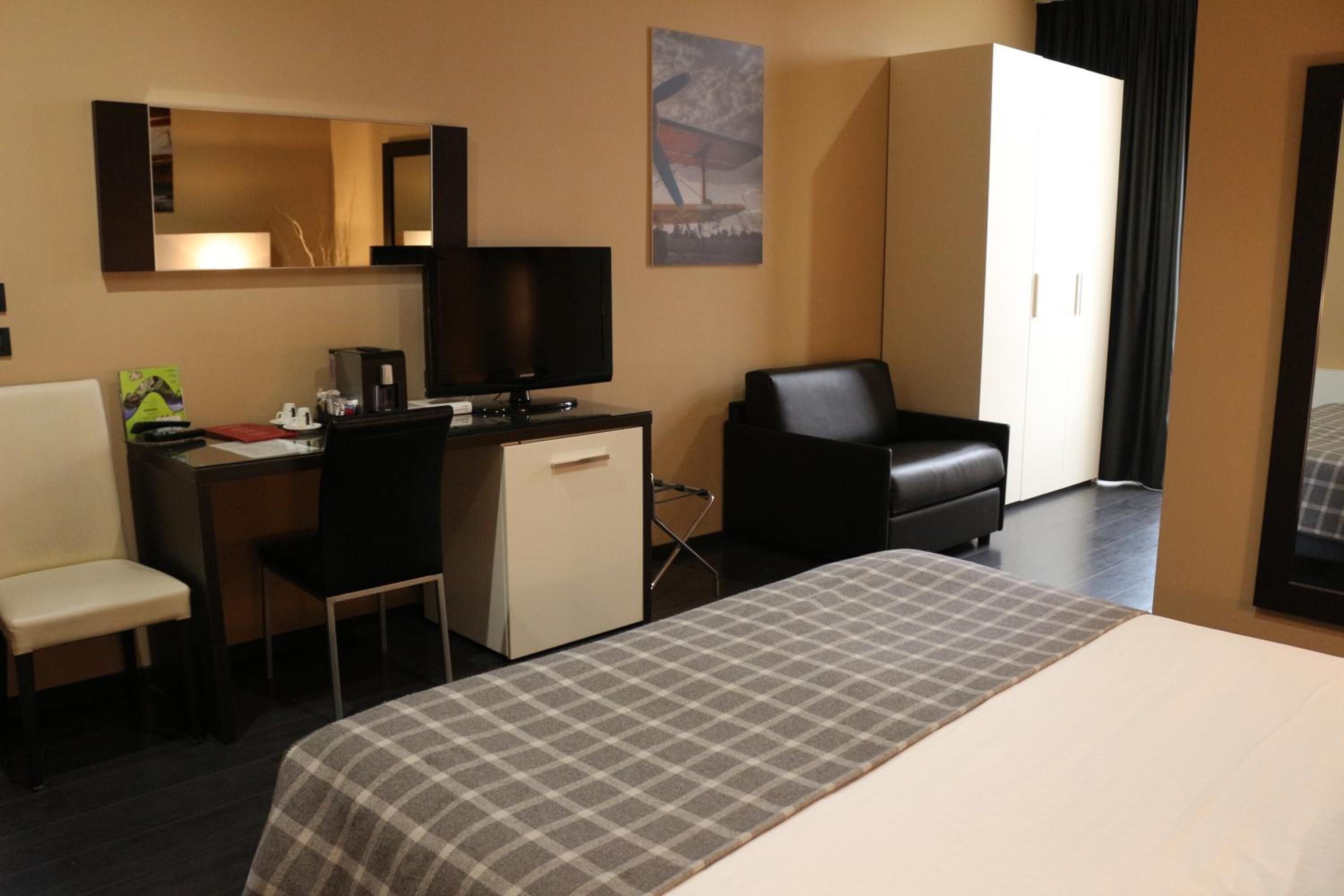 Una camera d'albergo con un letto, una scrivania con un computer, una sedia, un divano e un armadio.