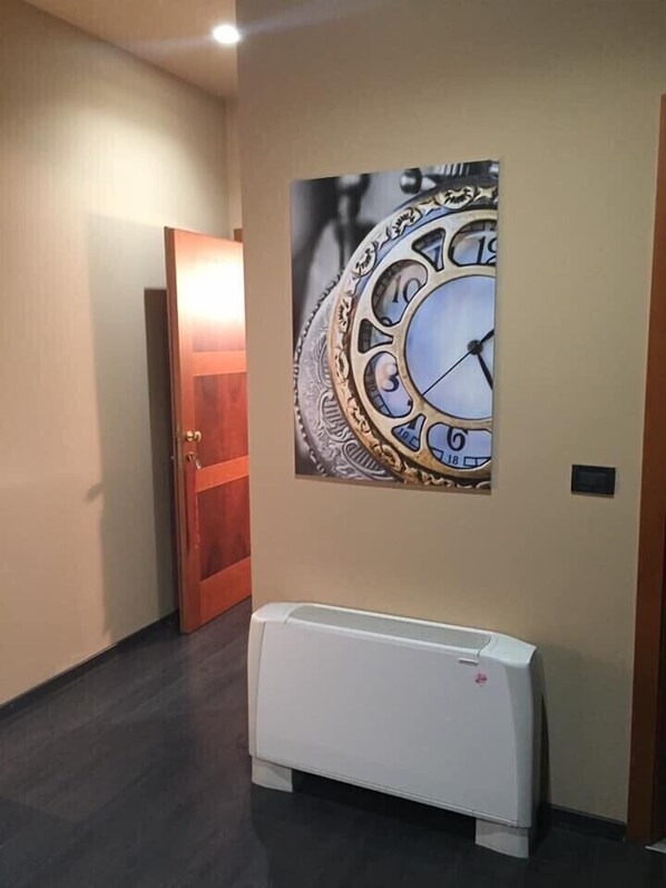 A hallway with a door, a wall-mounted clock, and a white radiator. - Hotel Garibaldi (Vercelli)