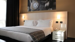 Habitación de hotel con una cama grande, una mesita de noche con lámpara y un reloj de pared.