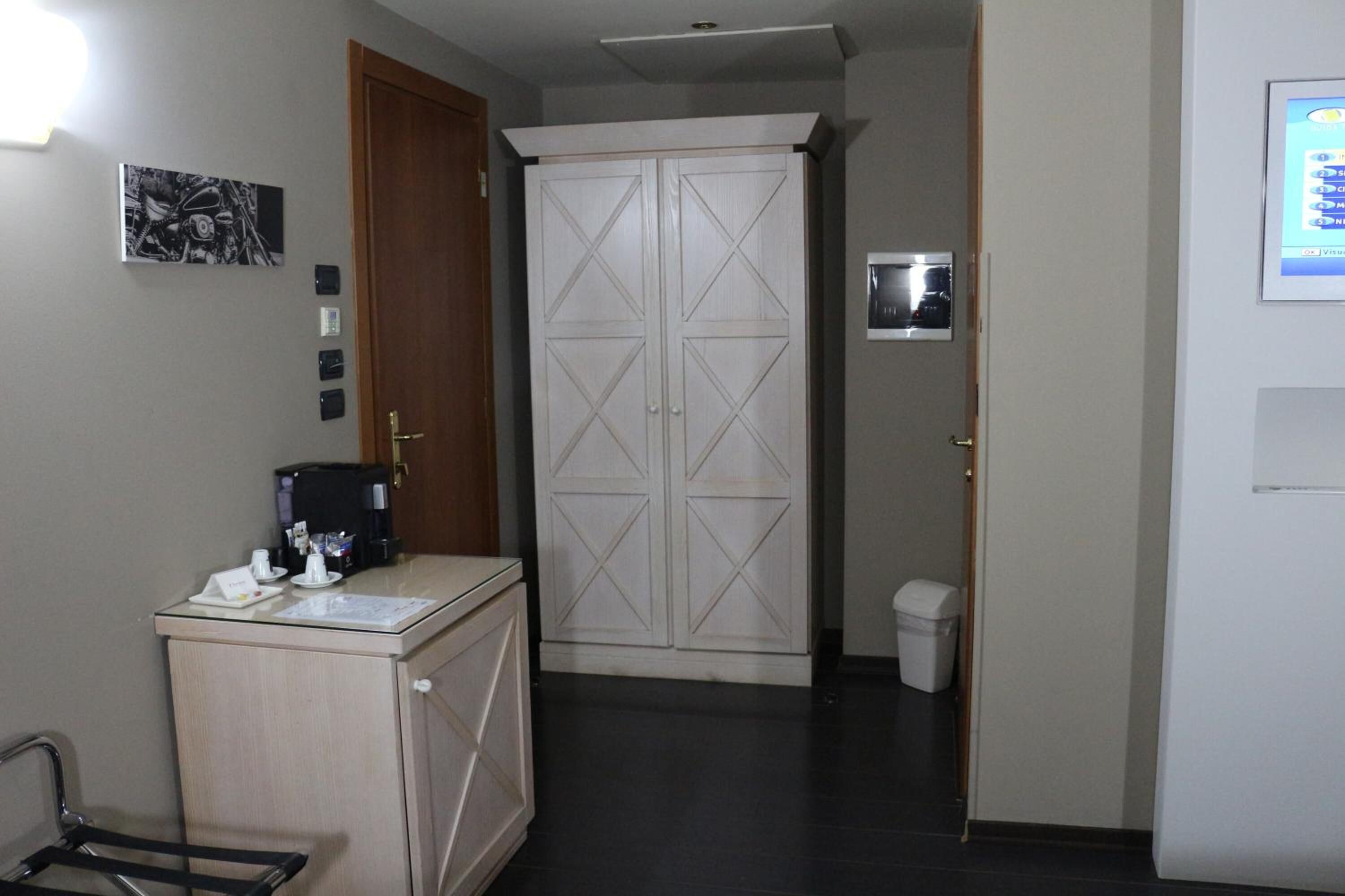 Habitación de hotel con minibar, armario, pequeño cesto de basura y termostato fijado a la pared.