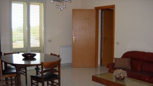 A dining area with a round table and chairs, a red sofa, and a coffee table with a vase. - Appartamenti a Pochi Passi dal Mare (Marsala)