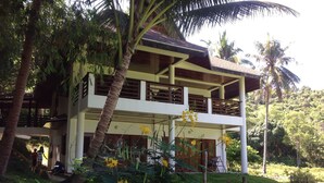 Un bâtiment à deux étages doté d’un balcon, entouré d’une végétation luxuriante et de palmiers.
