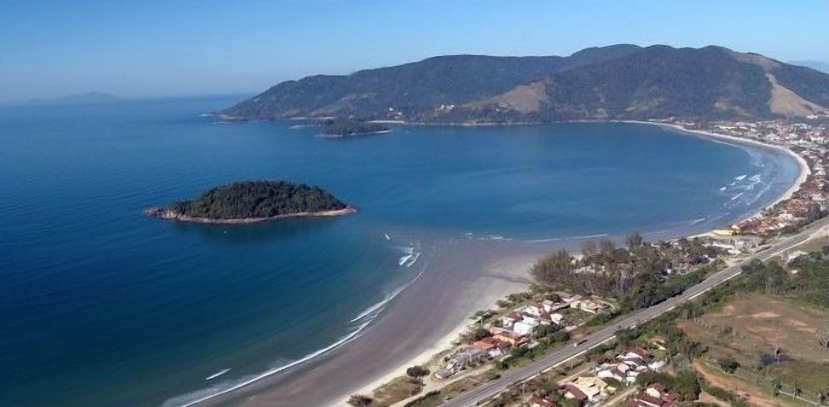 An aerial view of a coastal area with a beach, a small island, and a town with houses and roads.