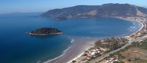 Une vue aérienne d’une zone côtière comprenant une plage, une petite île et une ville avec des maisons et des routes.