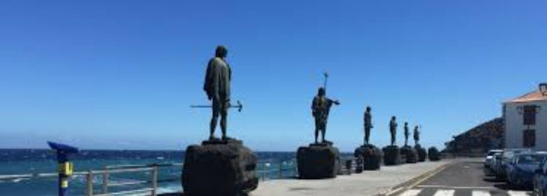 A coastal walkway with statues and a building in the background.