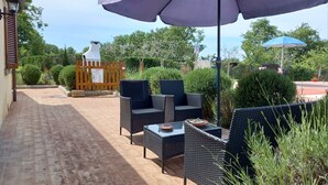 Eine Terrasse im Freien mit Korbmöbeln, einem Grill und einem großen Sonnenschirm, der Schatten spendet.