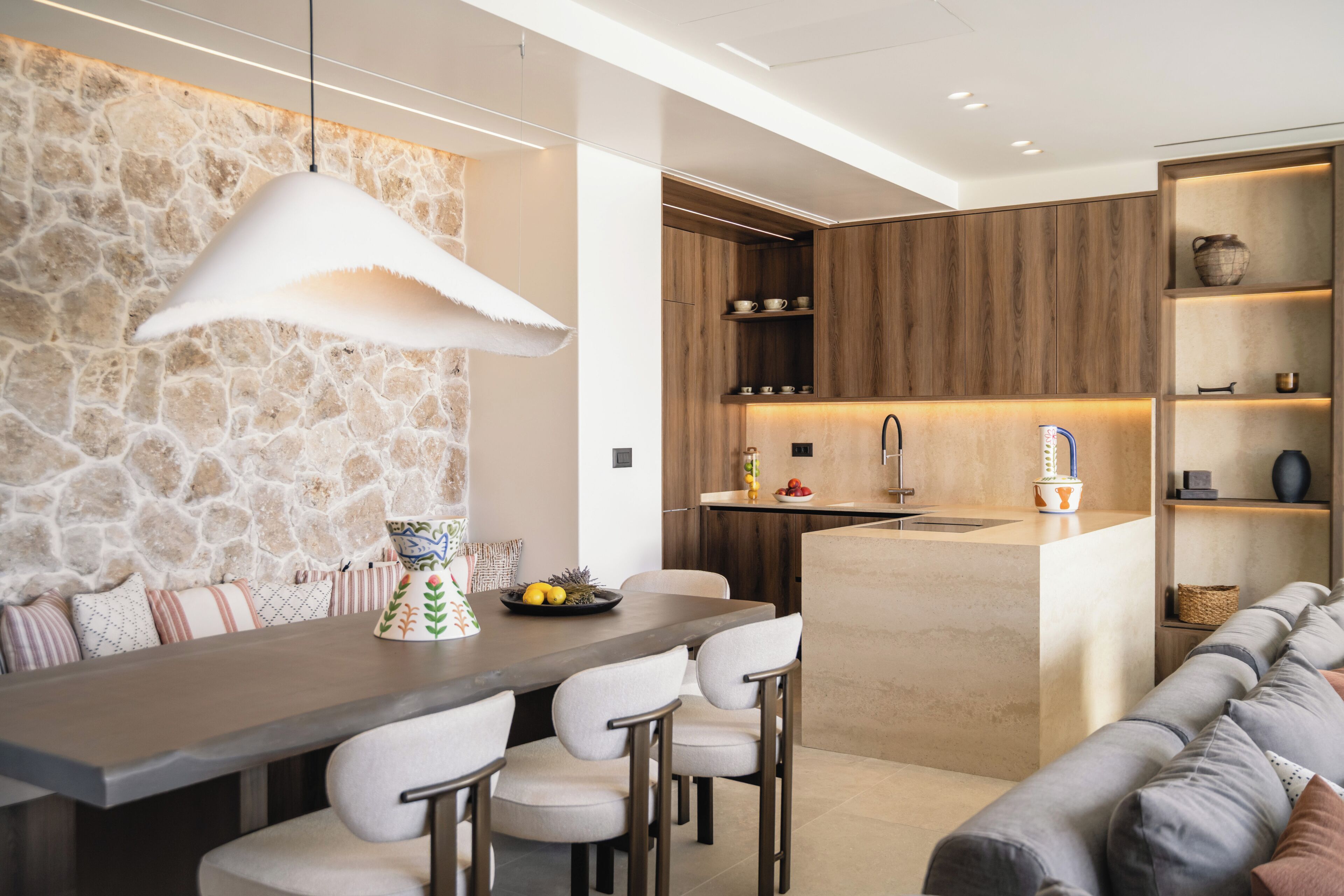 A modern kitchen with a stone accent wall, a built-in island with bar stools, and wooden cabinetry.