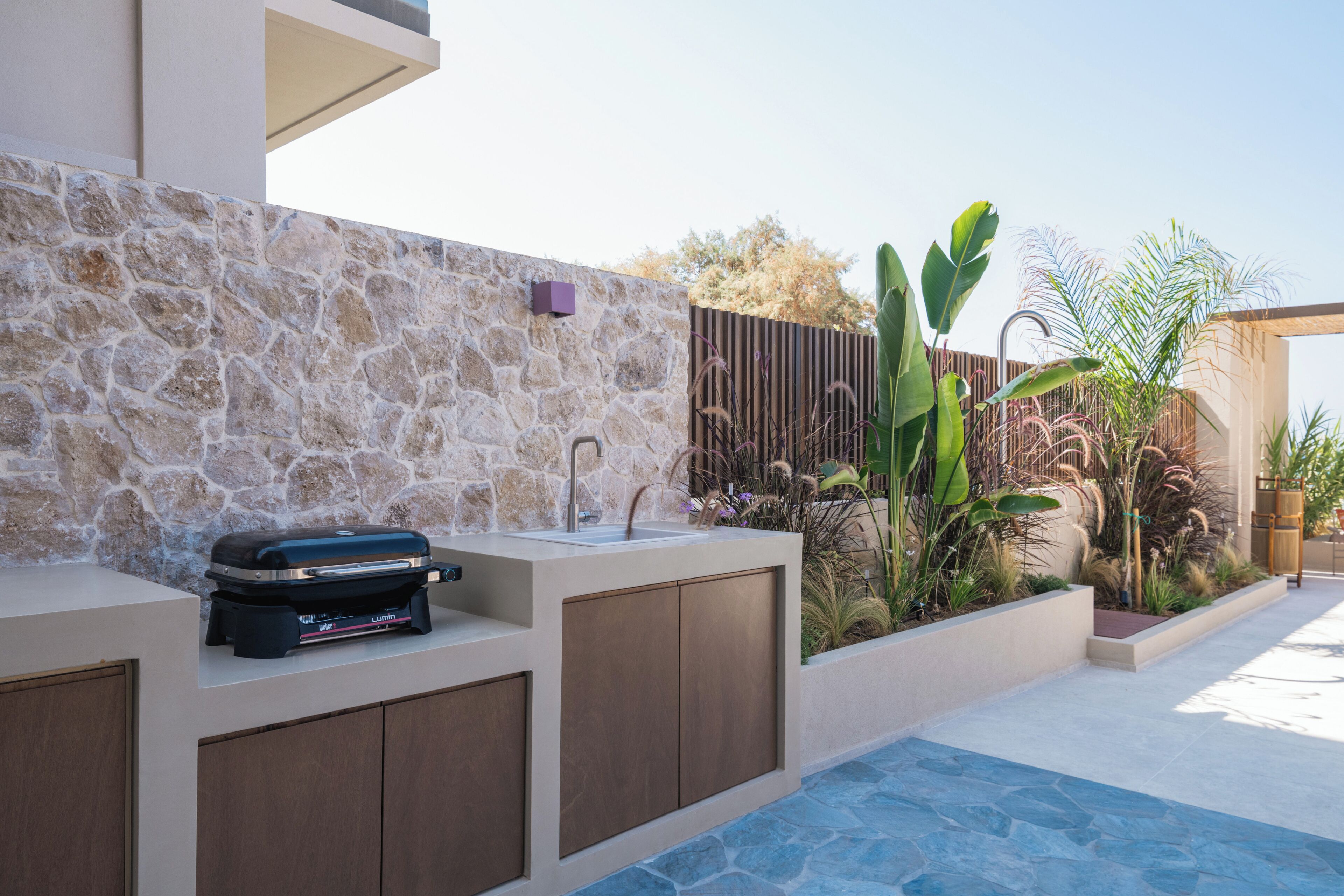 A modern outdoor kitchen with a stone wall, a barbecue grill, and a sink.