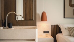 Une salle de bain moderne avec un lavabo en marbre, un miroir, une suspension lumineuse et une table de chevet avec un verre.