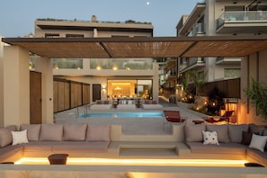 A modern outdoor pool area with a seating arrangement and a building in the background.