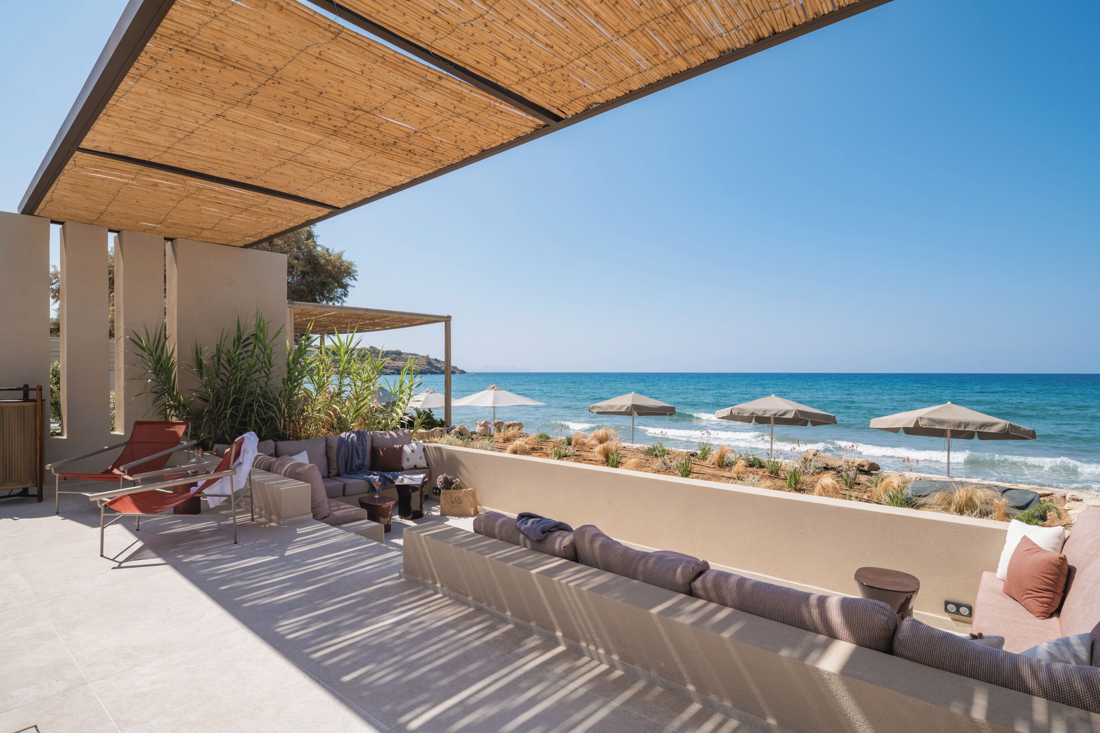 Une terrasse en bord de mer, dotée de sièges extérieurs, de parasols et offrant une vue sur l’océan.