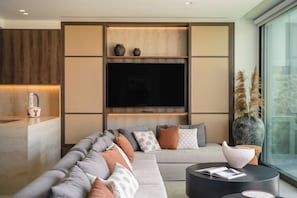 A modern living room with a sectional sofa, a flat-screen TV, and a large window. - Espera Beachfront Residence, Coastal City Living (Rethymno)