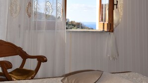 A room with a wooden ceiling, a window with a view, a wooden chair, and a bed with a patterned bedspread.