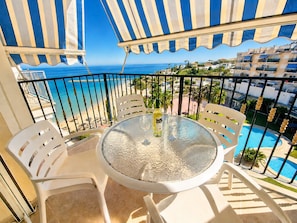 A balcony with a round table, white chairs, and a view of the sea and buildings.