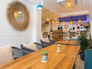 A restaurant with wooden tables, wicker chairs, and hanging pendant lights.