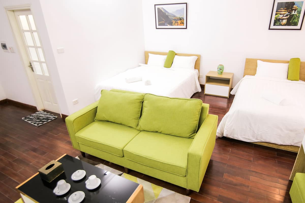 A hotel room with two beds, a green sofa, a small table with plates, and a door.