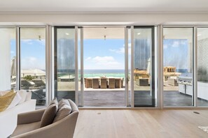 Un salón amplio con un gran ventanal corredera que da a un patio exterior con vistas al océano.