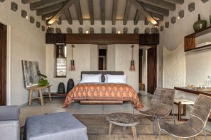 Une chambre spacieuse avec un grand lit, un bureau et des fauteuils en osier.